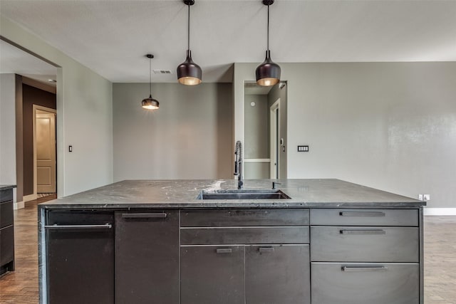 kitchen with dark stone countertops, baseboards, a sink, and wood finished floors