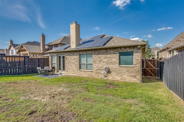 rear view of property with roof mounted solar panels, a patio area, a lawn, and brick siding