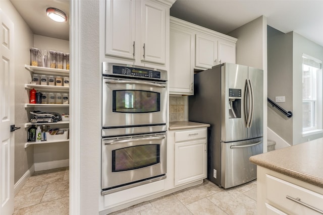 kitchen featuring baseboards, white cabinets, stainless steel appliances, light countertops, and backsplash