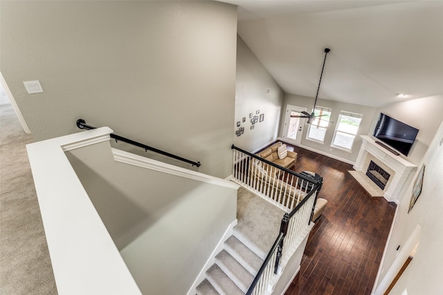 stairs with a fireplace with flush hearth, baseboards, and wood finished floors