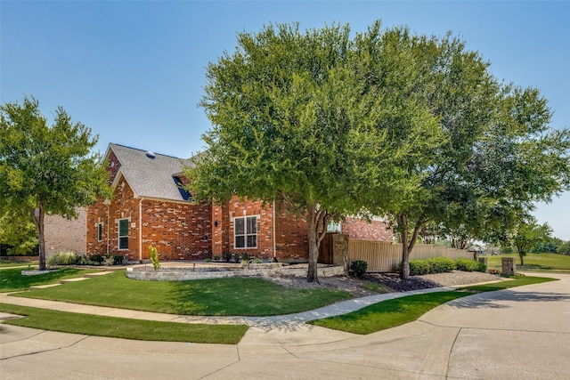 view of property hidden behind natural elements featuring brick siding, fence, and a front lawn