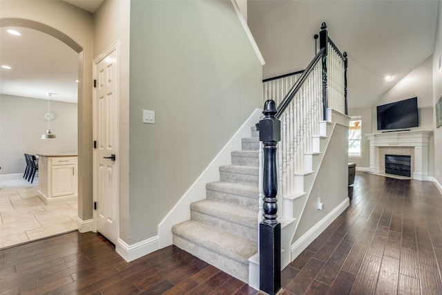 staircase with arched walkways, a fireplace, recessed lighting, wood finished floors, and baseboards