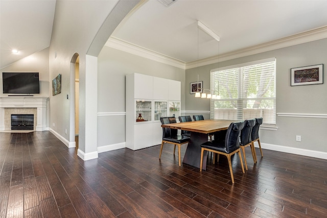 dining room featuring a fireplace with flush hearth, arched walkways, dark wood-type flooring, and ornamental molding