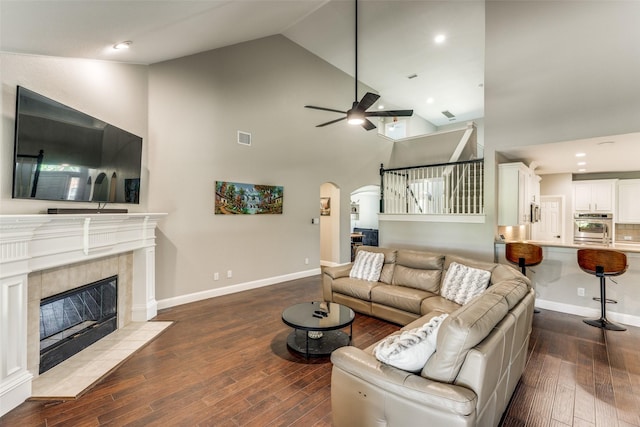 living area with arched walkways, ceiling fan, visible vents, hardwood / wood-style floors, and a tiled fireplace