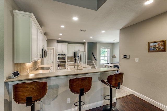 kitchen with a peninsula, appliances with stainless steel finishes, decorative backsplash, and a sink