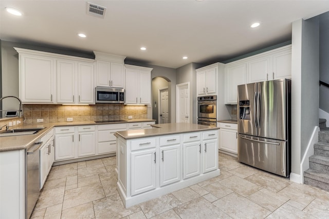 kitchen featuring arched walkways, a kitchen island, a sink, visible vents, and appliances with stainless steel finishes