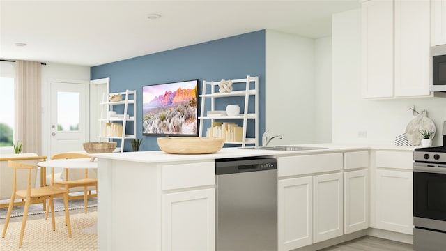 kitchen featuring stainless steel appliances, light countertops, white cabinets, a sink, and a peninsula