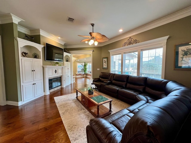 living area with ceiling fan, visible vents, ornamental molding, dark wood-style floors, and a glass covered fireplace