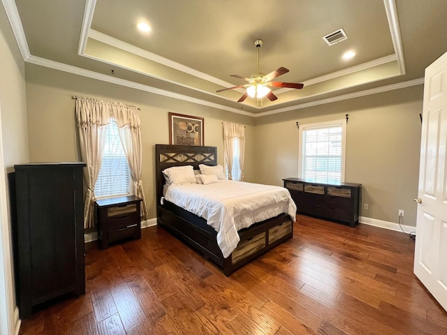 bedroom with dark wood-style floors, a tray ceiling, visible vents, and baseboards