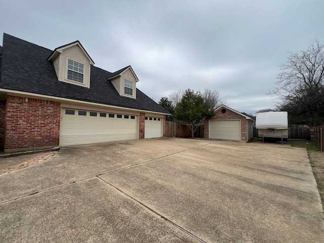 view of front facade with an outbuilding, brick siding, a shingled roof, fence, and a garage