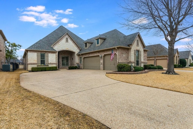 french country home with a garage, central AC, brick siding, concrete driveway, and stone siding