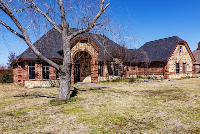 view of front facade with stone siding, brick siding, a front lawn, and roof with shingles