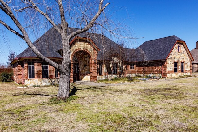 entrance to property featuring stone siding, brick siding, and roof with shingles