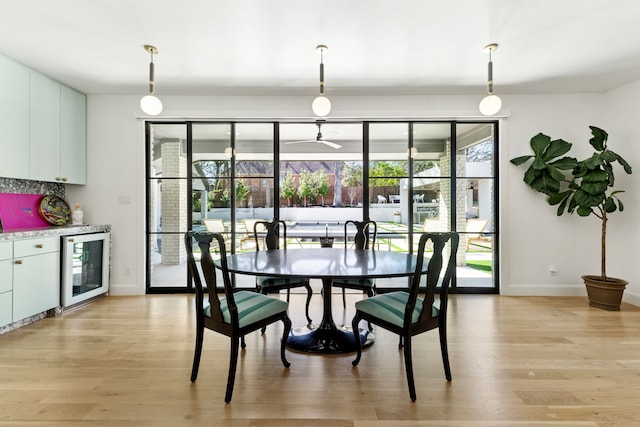 dining room with wine cooler, a dry bar, light wood-type flooring, and baseboards