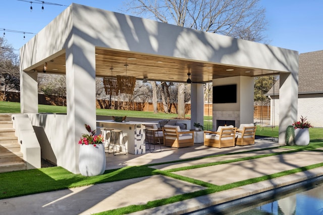 view of patio featuring fence, outdoor dry bar, a ceiling fan, and an outdoor living space with a fireplace