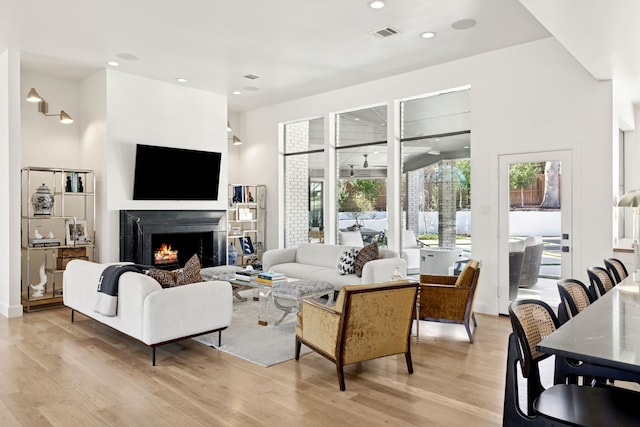 living room with visible vents, a healthy amount of sunlight, a warm lit fireplace, and light wood-style flooring