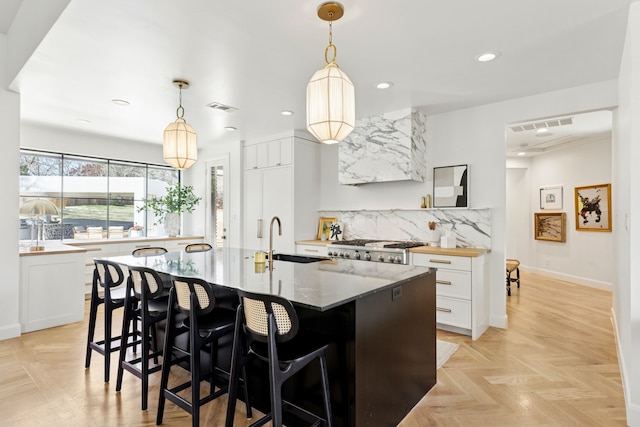 kitchen featuring visible vents, a kitchen bar, decorative backsplash, white cabinetry, and a sink