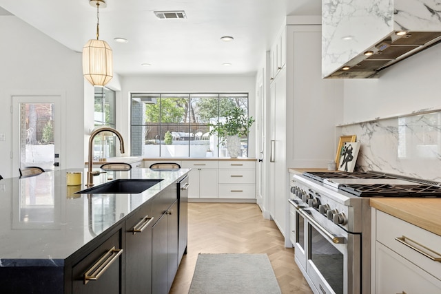 kitchen with light stone countertops, visible vents, range with two ovens, a sink, and tasteful backsplash