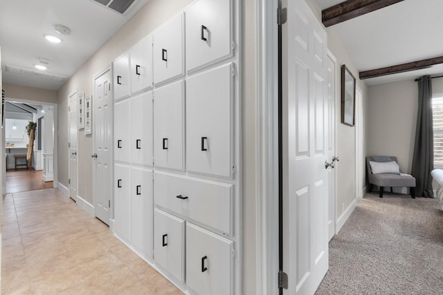 hallway featuring light carpet, visible vents, baseboards, and beam ceiling