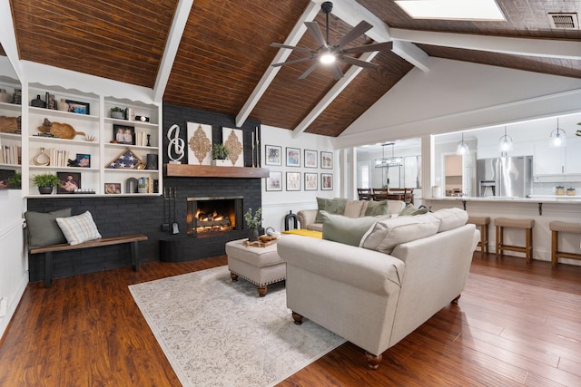 living area featuring dark wood-type flooring, a brick fireplace, ceiling fan, and beamed ceiling