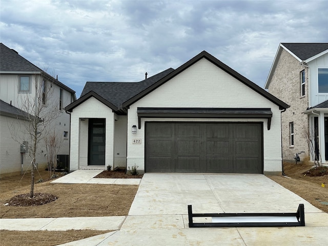 view of front of home featuring brick siding, roof with shingles, concrete driveway, central AC unit, and a garage