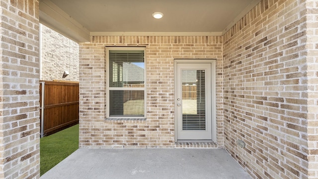 entrance to property with brick siding, a patio area, and fence