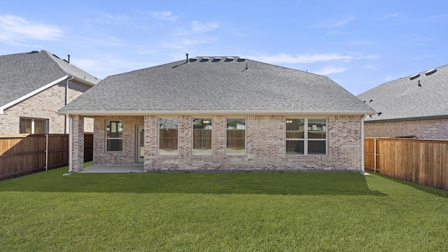 back of house featuring a fenced backyard, a yard, brick siding, a patio, and roof with shingles