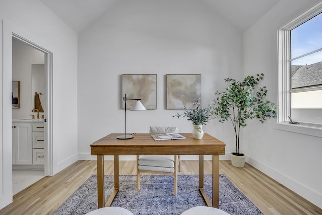 home office with lofted ceiling, a sink, light wood-style flooring, and baseboards