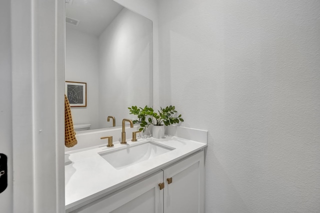 half bathroom with visible vents, a textured wall, vanity, and toilet