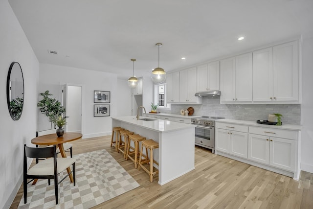 kitchen with stainless steel range, a sink, light wood-type flooring, white cabinetry, and backsplash