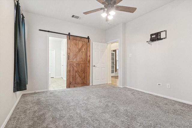 unfurnished bedroom featuring a barn door, baseboards, visible vents, a ceiling fan, and light colored carpet