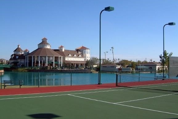 view of tennis court featuring community basketball court, a water view, and fence