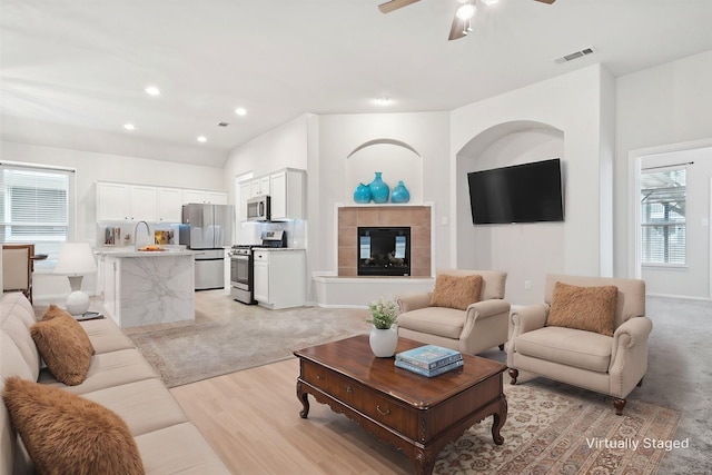 living room with ceiling fan, a tile fireplace, light wood-style flooring, recessed lighting, and visible vents