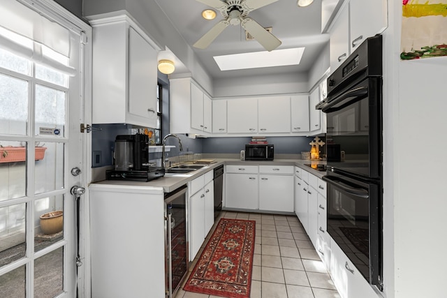 kitchen with a skylight, light tile patterned floors, a sink, beverage cooler, and black appliances