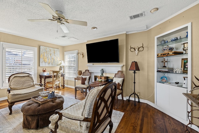 living room with built in features, visible vents, ceiling fan, wood finished floors, and crown molding