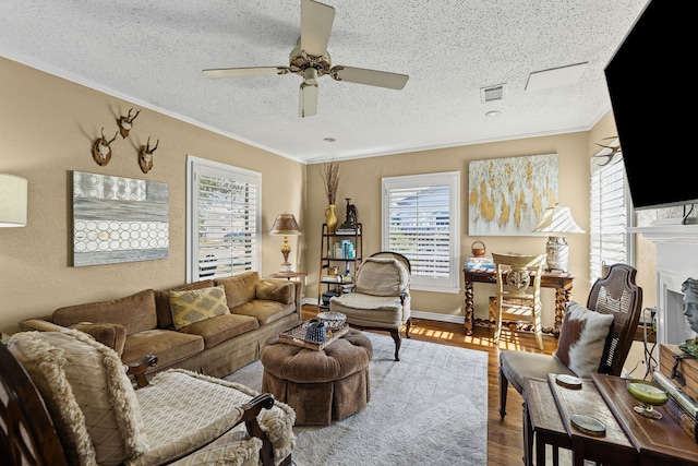 living area with visible vents, a fireplace with raised hearth, ceiling fan, ornamental molding, and wood finished floors