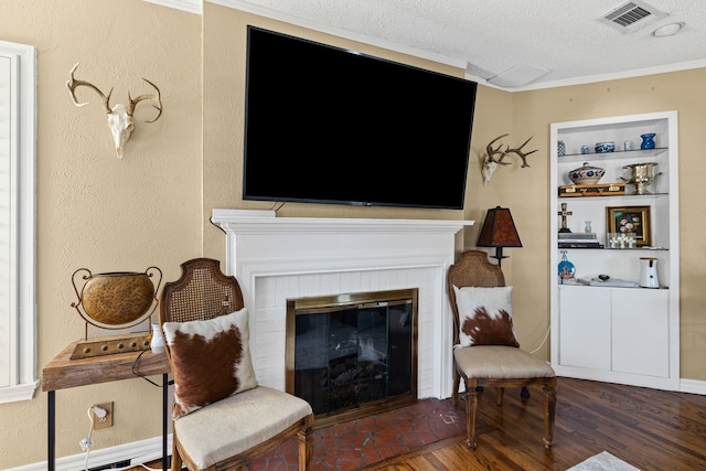 living room featuring a textured ceiling, a fireplace, wood finished floors, visible vents, and built in features