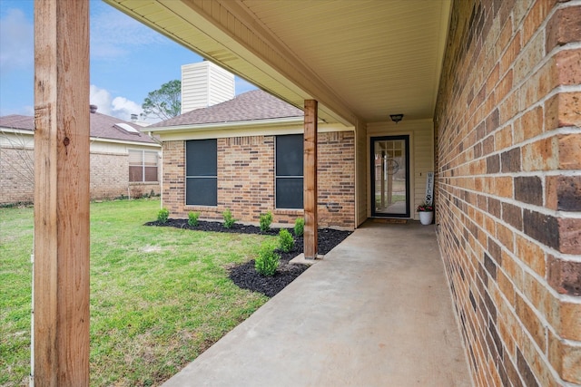 doorway to property with a shingled roof, a lawn, and brick siding