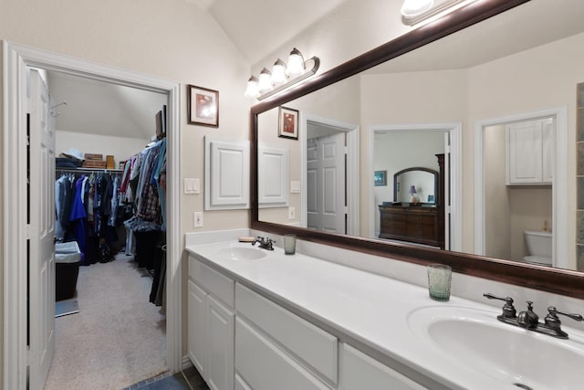 bathroom with double vanity, a spacious closet, vaulted ceiling, and a sink