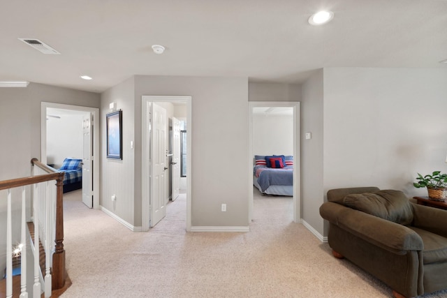 hall with baseboards, an upstairs landing, visible vents, and light colored carpet