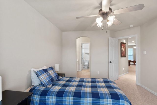 bedroom with baseboards, arched walkways, light colored carpet, ceiling fan, and ensuite bathroom