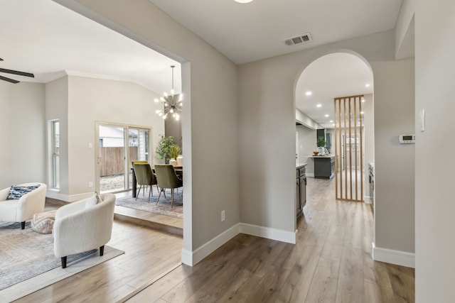 hallway with arched walkways, wood finished floors, visible vents, and baseboards