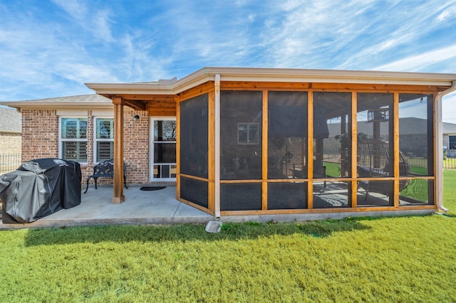 rear view of property with a patio, a yard, brick siding, and a sunroom