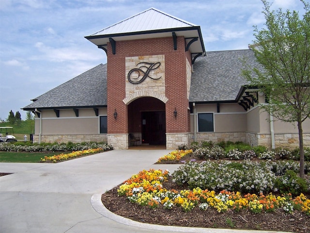 view of front of house with stucco siding, driveway, stone siding, a shingled roof, and metal roof