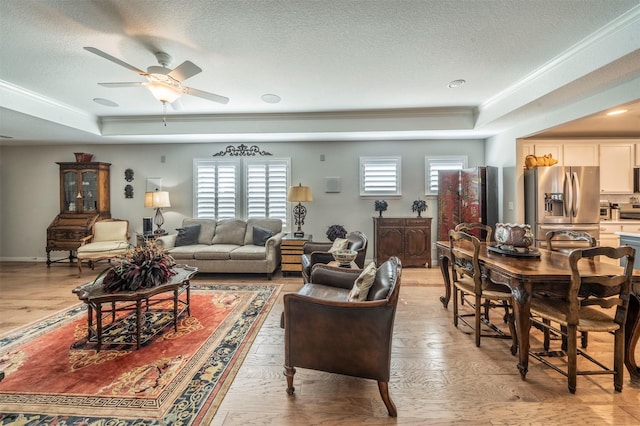 living area featuring a ceiling fan, baseboards, crown molding, a textured ceiling, and a raised ceiling