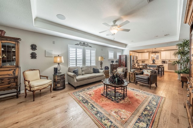 living area featuring crown molding, ceiling fan, a tray ceiling, light wood-style floors, and a textured ceiling