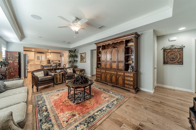 living area featuring a tray ceiling, light wood-style flooring, crown molding, and visible vents