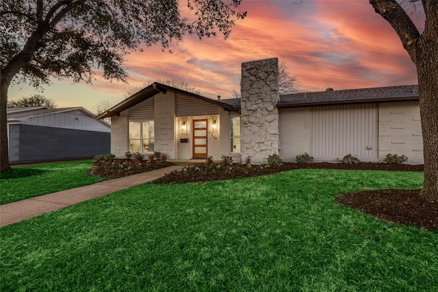 mid-century modern home with brick siding, a shingled roof, a chimney, and a yard