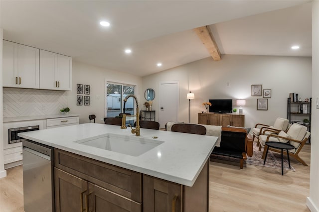 kitchen with appliances with stainless steel finishes, a sink, lofted ceiling with beams, and light wood finished floors