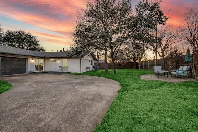 yard at dusk featuring a patio area, driveway, an attached garage, and fence